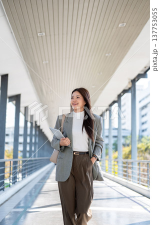Pretty asian woman student office worker holding tablet as walking with hand in pocket on footbridge 137753055