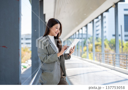 Happy asian woman student office worker looking at tablet standing leaning on railing of footbridge. 137753058