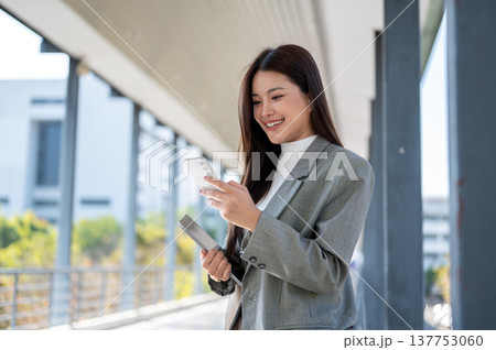 Asian woman student office worker looking at phone holding tablet standing or walking on footbridge. 137753060
