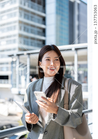 Pretty asian woman student office worker holding tablet and phone walking on bridge with cityscape. 137753063