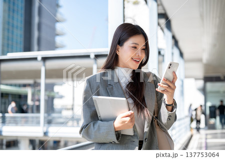 Pretty asian woman student office worker holding tablet looking at phone and standing on footbridge. 137753064