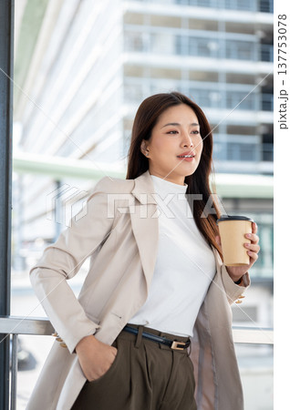 Pretty asian woman office worker holding coffee standing hand in pocket on footbridge with cityscape 137753078