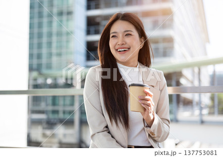 Happy asian woman office worker holding coffee cup standing aside railing on bridge with cityscape. Happy asian woman office worker holding coffee cup standing aside railing on bridge with cityscape. 137753081