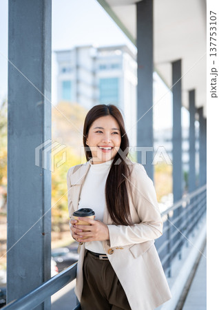 Pretty asian woman office worker holding coffee with both hands as standing or walking on footbridge 137753107