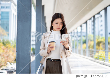 Pretty asian woman office worker holding coffee looking at phone standing or walking on a footbridge 137753108