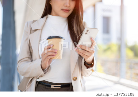 Close up of asian woman office worker holding coffee looking at phone standing walking on footbridge Close up of asian woman office worker holding coffee looking at phone standing walking on footbridge 137753109