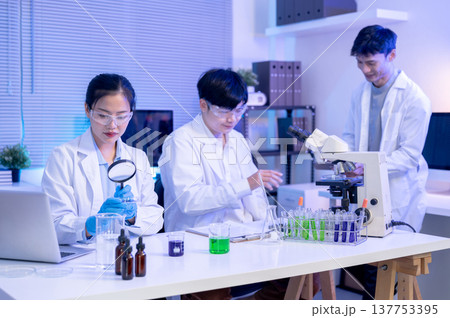 Woman scientist researcher holding magnifying glass look at test sample aside coworkers in lab room. Woman scientist researcher holding magnifying glass look at test sample aside coworkers in lab room. 137753395