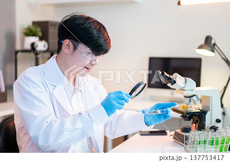 Scientist researcher man using magnifying glass look at test sample on dish aside microscope in lab. Scientist researcher man using magnifying glass look at test sample on dish aside microscope in lab. 137753417