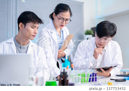 Woman scientist researcher looking at test subject with colleague or student as working in lab room. 137753432