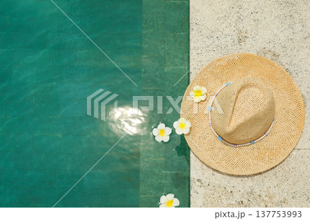 A straw hat rests by the pool with flowers floating nearby 137753993
