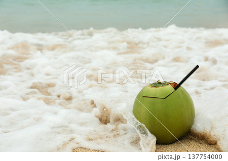 A coconut drink sits on the sand near the ocean waves A coconut drink sits on the sand near the ocean waves 137754000