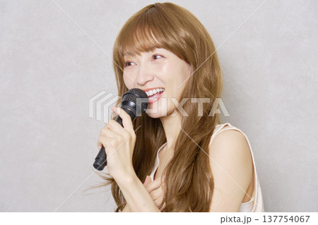 マイクを持って歌うミドルエイジの女性　ポートレート　グレー背景 137754067