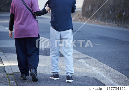 朝の都市の住宅地で歩く介護職員とシニア男性の姿	 137754122