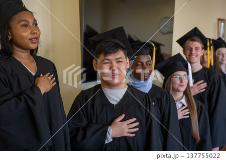 Graduates stand proudly at the ceremony with their hands over their hearts.  137755022