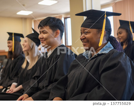 Young people in graduation gowns listen to a speech by a classmate.  137755029