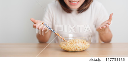Happy young Asian woman enjoying a delicious bowl of hot instant noodles while relaxing at home, Cheerful female eating instant ramen with a smile at apartment. Simple lifestyle and quick meal concept 137755186