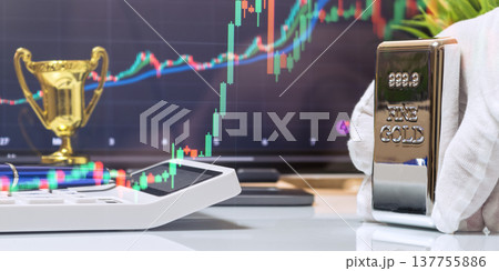 Gold Bar on Desk with Trophy and Rising Financial Chart 137755886