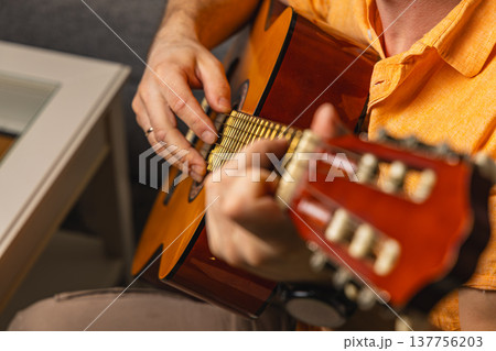 Person plays guitar in a cozy indoor setting during the day 137756203