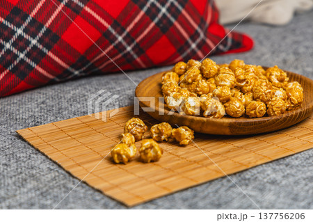 Popcorn sits on a wooden plate on a mat next to a plaid pillow in a cozy space Popcorn sits on a wooden plate on a mat next to a plaid pillow in a cozy space 137756206