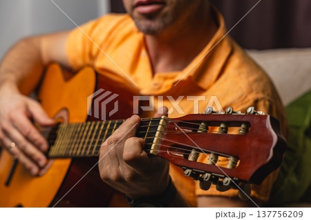 Man plays guitar at home during evening hours with focus on hands 137756209