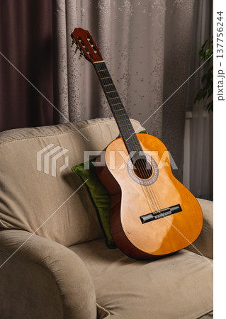 Guitar resting on a sofa in a room with curtains and a plant Guitar resting on a sofa in a room with curtains and a plant 137756244