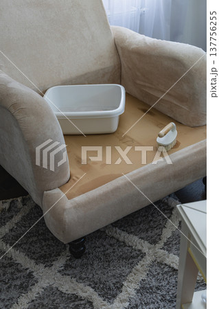 Cleaning supplies on a chair with a light fabric cover and patterned rug 137756255