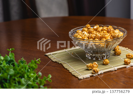 Popcorn in a clear bowl placed on a bamboo mat on a wooden table 137756279