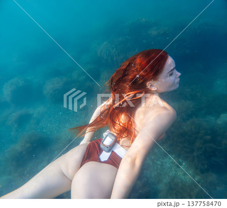 Woman diving redhead young woman with long red hair swimming underwater in clear blue ocean water during a serene summer vacation 137758470