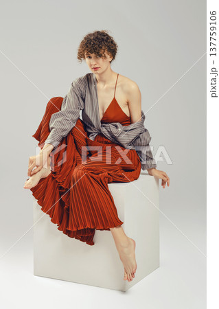 Stylish woman sits gracefully on a white cube against a neutral background 137759106