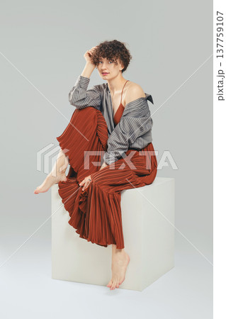 Elegant barefoot woman in stylish outfit sitting on studio cube 137759107