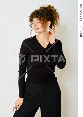 Stylish woman with curly hair poses in black sweater and trousers against a neutral backdrop 137759126