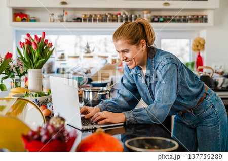 Mature woman searching recipe online on laptop while cooking in kitchen. 137759289