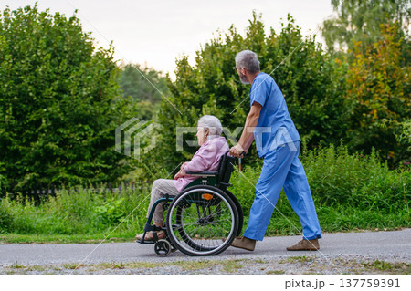 Senior patient and male nurse talking during walk outdoors. Senior patient and male nurse talking during walk outdoors. 137759391