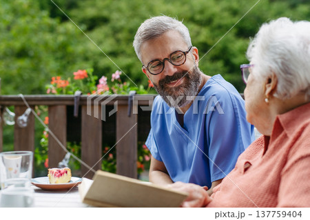 Caregiver spending time with elderly woman, reading book. Caregiver spending time with elderly woman, reading book. 137759404