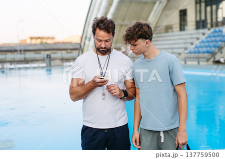 Coach giving advice to young swimmer, walking by pool. 137759500