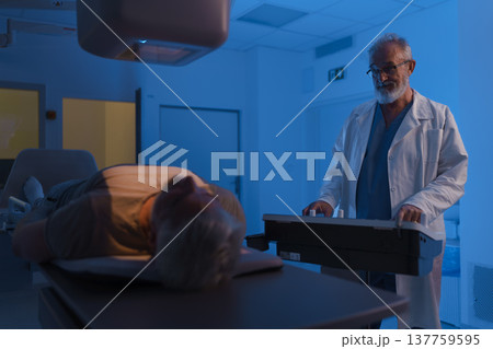 Male patient undergoing X-ray examination using tilting radiographic wall stand. Male patient undergoing X-ray examination using tilting radiographic wall stand. 137759595