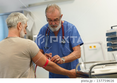 Older doctor drawing blood from patient's arm. Older doctor drawing blood from patient's arm. 137759616