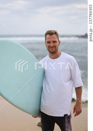 Cheerful Surfer Standing By Shoreline. Casual Surfer Smiling Near Gentle Ocean Waves And Trees Cheerful Surfer Standing By Shoreline. Casual Surfer Smiling Near Gentle Ocean Waves And Trees 137760303