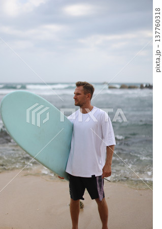 Serene Caucasian Man Wearing White Shirt Leaning On Surfboard Overlooking Rugged Shoreline And Textured Sea Serene Caucasian Man Wearing White Shirt Leaning On Surfboard Overlooking Rugged Shoreline And Textured Sea 137760318