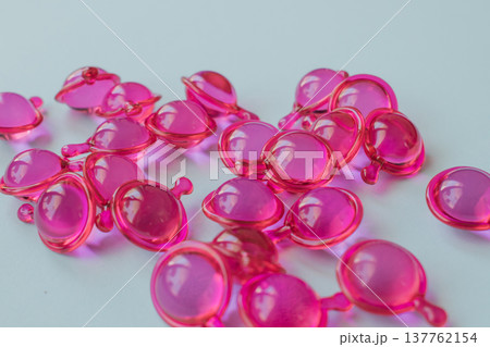 Close-up macro shot of many glossy pink hair treatment capsules. Focused foreground highlights the rich oil and reflective texture Close-up macro shot of many glossy pink hair treatment capsules. Focused foreground highlights the rich oil and reflective texture 137762154