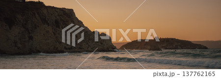 Golden orange sunset sky over ocean waves near steep coastal cliff and rocky island landscape view 137762165