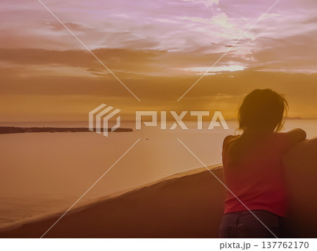 Young girl on a terrace observing the magical sunset over the Aegean Sea and the volcanic caldera of Santorini, Greece Young girl on a terrace observing the magical sunset over the Aegean Sea and the volcanic caldera of Santorini, Greece 137762170