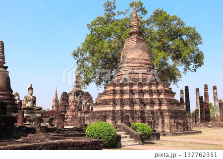 Ancient stone stupa and Buddha statue, Wat Mahathat, Sukhothai historical park. Picturesque scene with old stupa, Sukhothai old city, Northern Thailand. Topic of vacation, travel, trip, cruise, tour Ancient stone stupa and Buddha statue, Wat Mahathat, Sukhothai historical park. Picturesque scene with old stupa, Sukhothai old city, Northern Thailand. Topic of vacation, travel, trip, cruise, tour 137762351