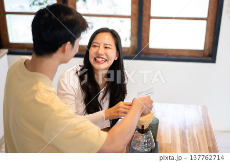 Asian man holding woman's hand pouring powder in dripper while making coffee. Couple in the kitchen. Asian man holding woman's hand pouring powder in dripper while making coffee. Couple in the kitchen. 137762714