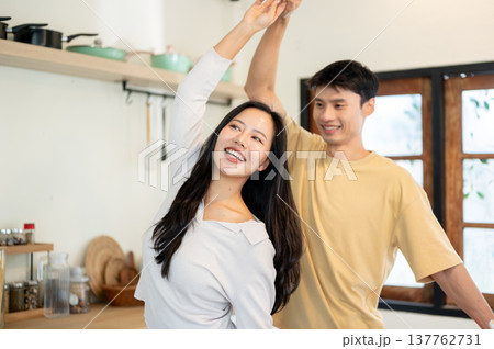 Pretty asian woman and a man couple holding hands dancing or spinning aside kitchen cooking counter. Pretty asian woman and a man couple holding hands dancing or spinning aside kitchen cooking counter. 137762731