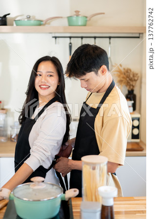 Asian couple a man tying apron for woman girlfriend before cooking food standing at kitchen counter. 137762742
