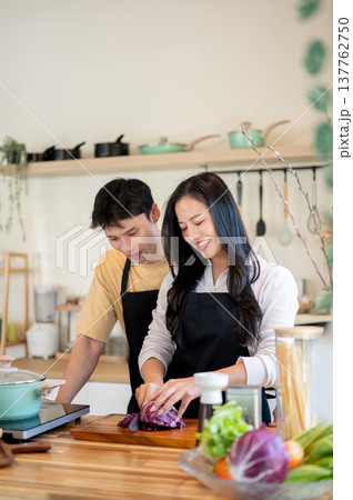 A man looking teaching woman girlfriend cooking food while standing at kitchen counter. Asian couple A man looking teaching woman girlfriend cooking food while standing at kitchen counter. Asian couple 137762750