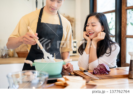 Asian couple a happy woman girlfriend looking at man boiling spaghetti at kitchen cooking counter. Asian couple a happy woman girlfriend looking at man boiling spaghetti at kitchen cooking counter. 137762764