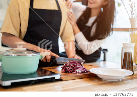 Close up of couple a woman clinging to boyfriend cutting vegetable while cooking at kitchen counter 137762773
