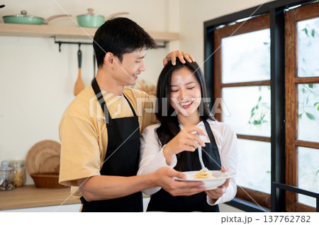 Asian couple man boyfriend patting head of woman girlfriend while cooking eating at kitchen counter. 137762782